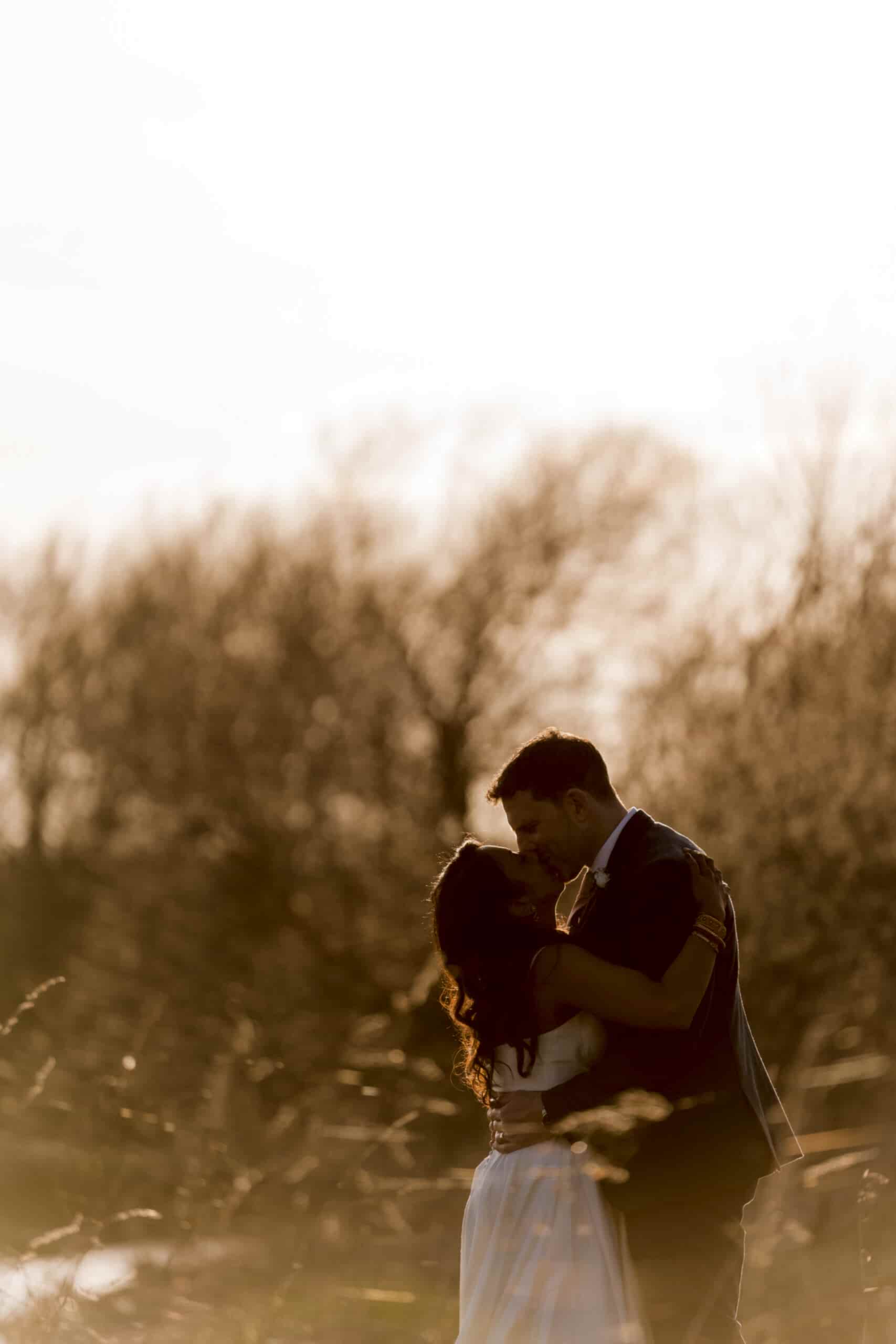A couple embracing in a loving moment backlit by a warm sunset.